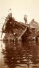 A photo of two men standing on top of a ship wreck in the water. Only part of the hull is visible.