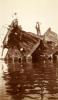 Une photo de deux hommes debout sur le dessus d’une épave de bateau dans l’eau. Seule une partie de la coque est visible.