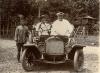 William McRae sitting in a car with a local man at the wheel. Another man stands to the side.  