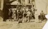 A photo of a group of men standing in front of the base of a wooden derrick. There are two International Drillers standing in the front, wearing white outfits and pith helmets.