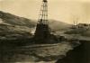 A photo of an oil rig with four legs on a dirt hill. The bottom part has been covered in dark cloth. There are piles of casing around the sides of the rig.