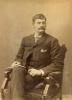 A photo of Thomas Knapp. He is sitting in an arm chair with a plush seat and arm rests. He is holding a folded piece of paper and is wearing a dark suit with the top button of his jacket done up.