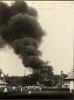 A photo of a group of people watching a cloud of black smoke near a group of oil derricks.