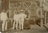 William McRae standing with two men, all in white suits, in front of three stretched tiger skins.  