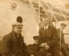 A photo of four men sitting at the base of a set of metal stairs on a boat deck. They are wearing dark jackets. 