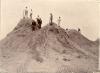 A photo of nine men standing on top of a dirt hill. Four are holding rifles.