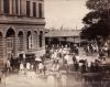 A photo of a crowded street outside of a large building near the waterfront.  