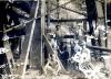 Two International Drillers standing behind six seated labourers inside of an oil rig. There are metal and wood beams around them.