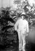 Henry Gregory standing in front of a trees. He is wearing a white suit and pith helmet. 