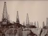 Oil field in Myanmar with many derricks, and local labourers scattered around the scene.