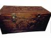 The front of a carved cedar chest. There are scenes carved into the lid and side showing people, trees, and buildings. There are golden corners and openers on the box. 