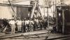 Two International Drillers wearing white and eight labourers in work clothes standing in front of a rig. There is a pile of casing in front of them.  