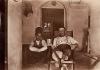 A photo of Humphrey Tracy laying back in a chair with a glass in his hand. There is a boy squatting beside him. 