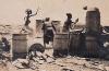 Five people surrounded by barrels and shoveling cement to build up a well. 