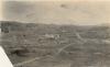 A photo of a road stretching through a desert, with hills in the background. There is a building in the middle of the photo. 