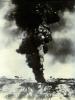 A billowing black cloud of smoke rising off of a hill. There are a few trees in the background.