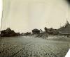 A photo of a group of buildings sitting on an embankment on either side of a sandy road. The buildings on the left and right have tiered roofs.