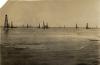 A photo of water washing over the bottoms of oil derricks that are built on a sandy beach. 