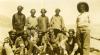 A photo of an International Driller wearing a white shirt, standing next to ten local workers wearing hats.