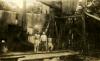 Three men standing in front of an oil rig covered with metal siding. They are standing on a pile of casing.