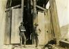 Two men wearing dark clothing standing in front of an opening in a rig covered with wooden planks.