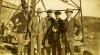 A photo of five International Drillers standing at the base of an oil derrick. They are wearing suits and hats.