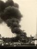 A photo of a group of people watching a cloud of black smoke near a group of oil derricks.